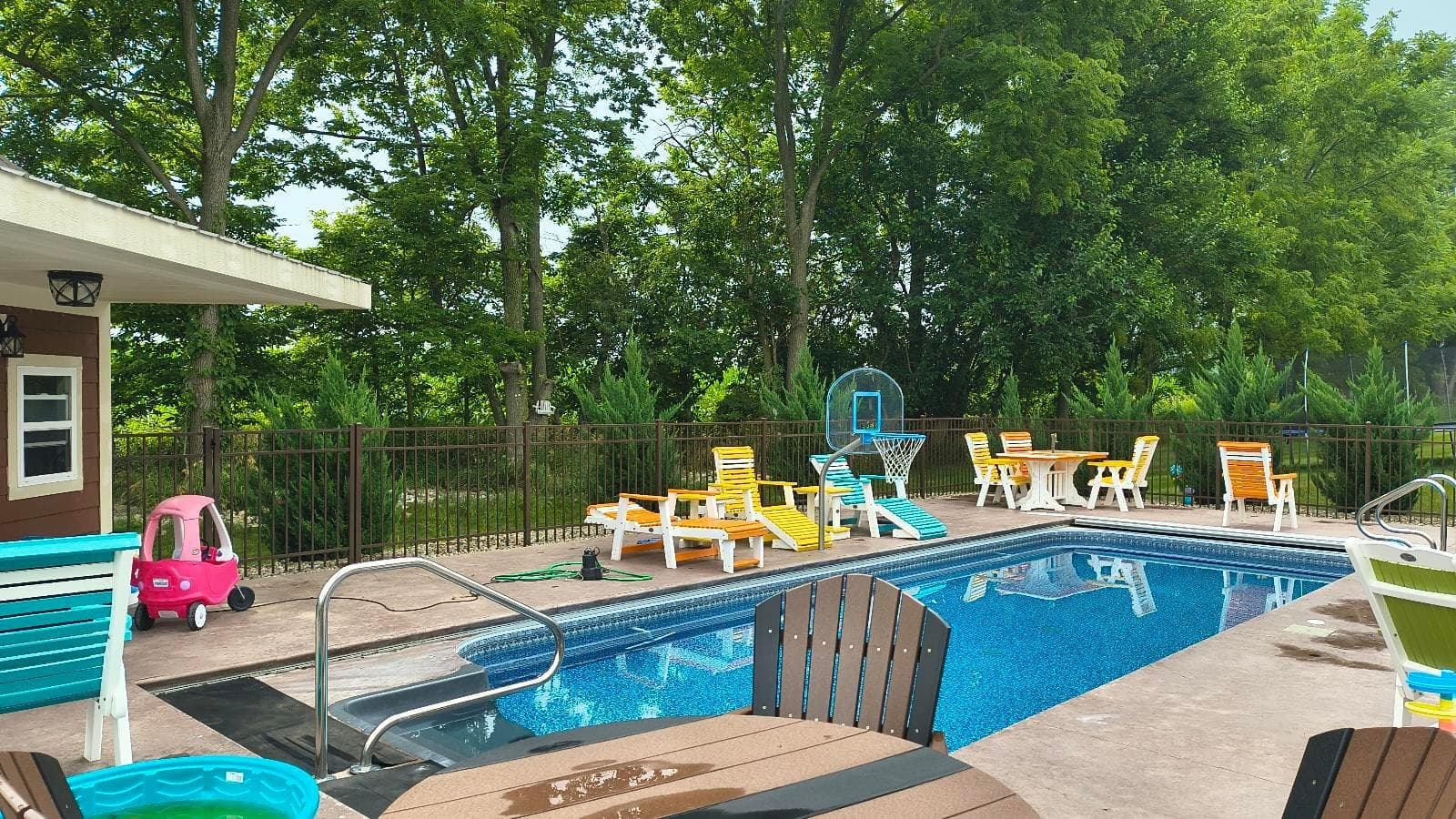 Black aluminum fencing borders a pool area with chairs and a deck.