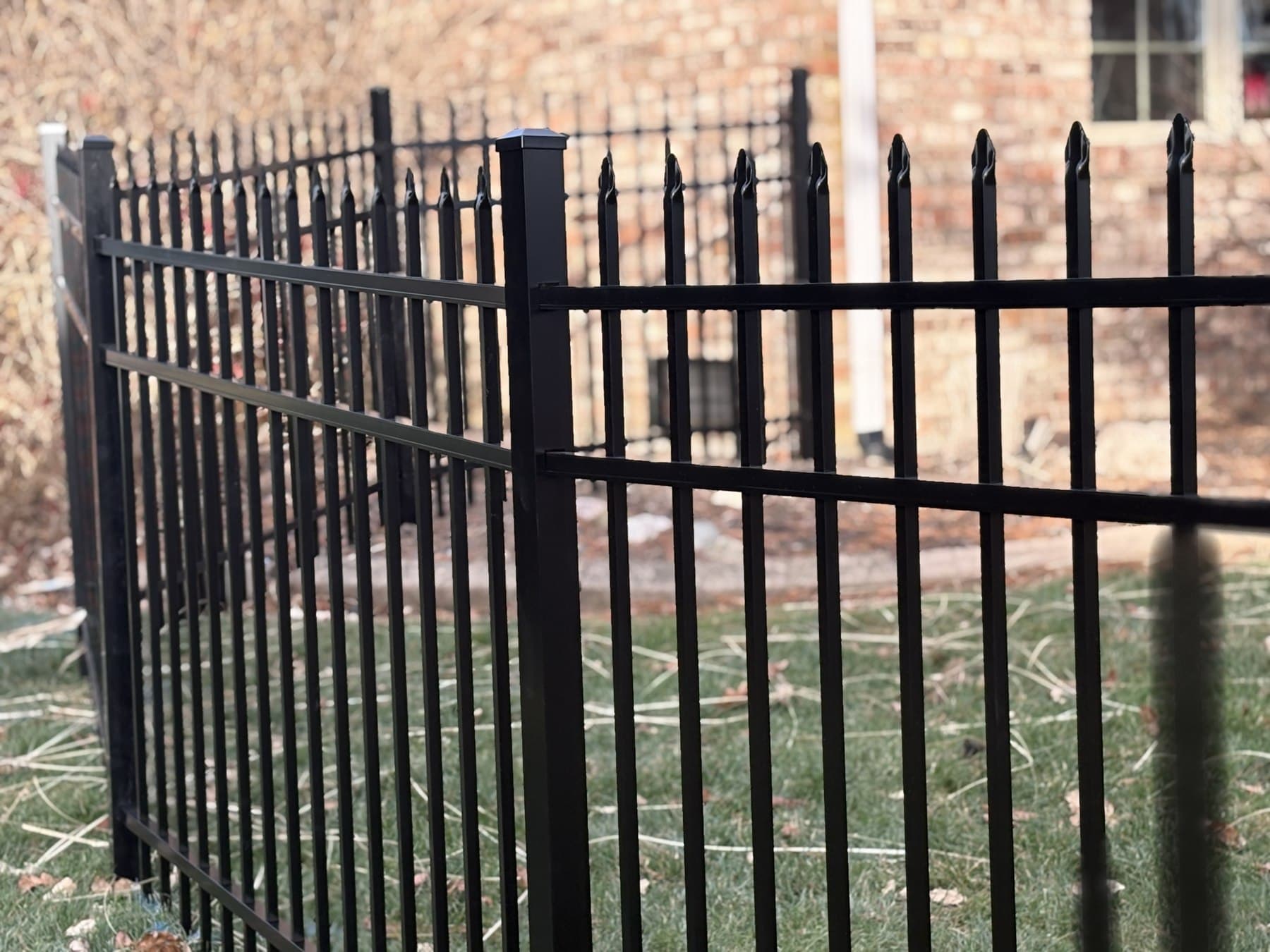 Pointed black pickets and horizontal rails stand beside a brick wall.