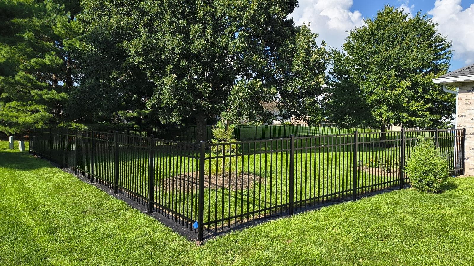 Black aluminum fencing makes a corner in a green lawn beneath trees.