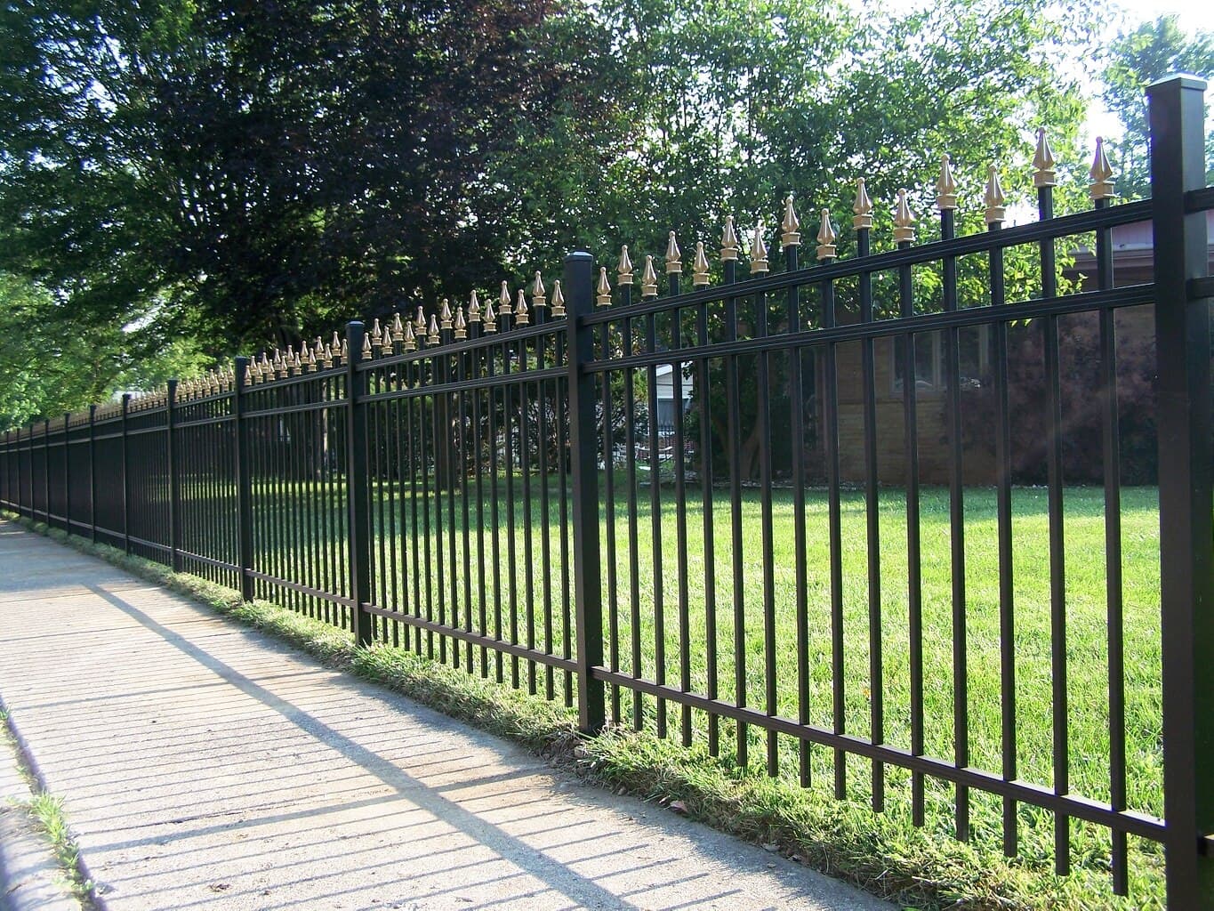 Black aluminum fencing runs alongside a paved driveway.