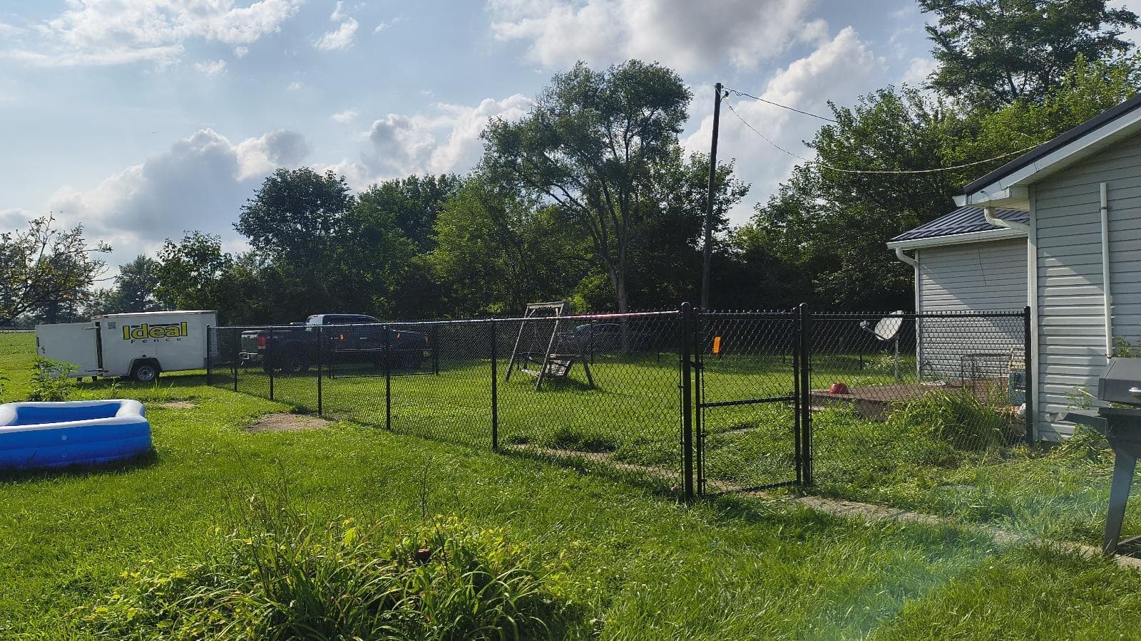 Black chain-link fencing separates neighboring lawns beneath mature trees.