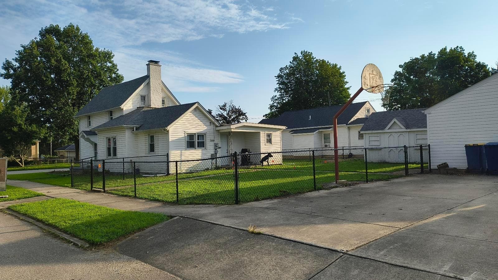 Black chain-link fencing wraps a lawn beside the sidewalk and house.
