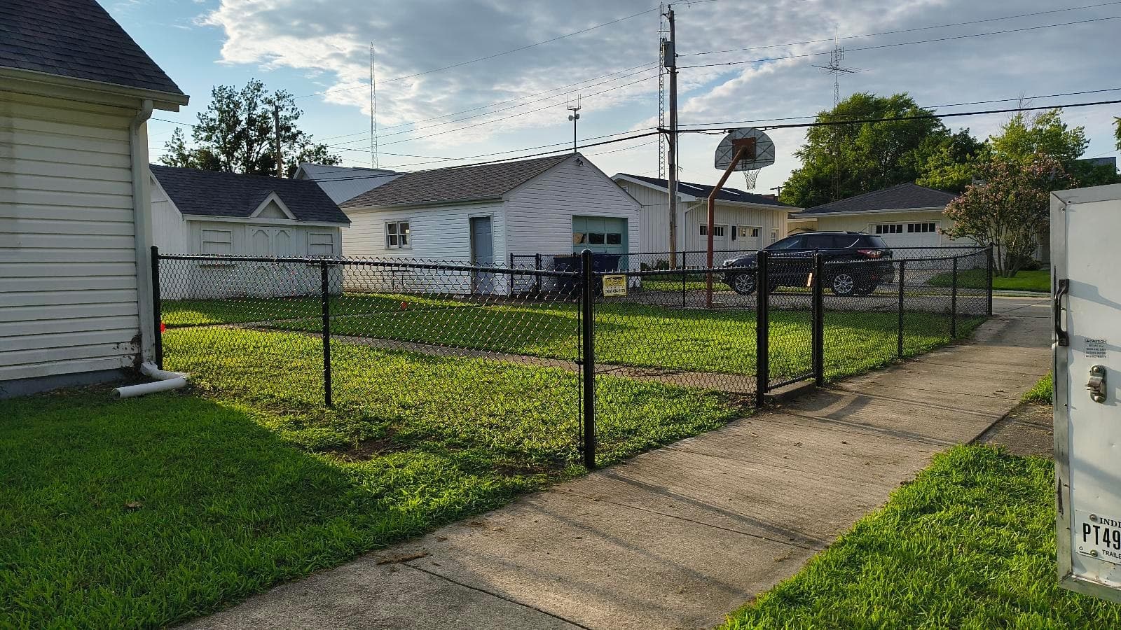 A chain-link corner defines the grass beside a house and driveway.