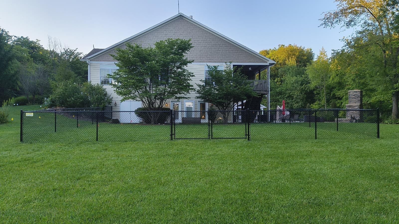 Chain-link fencing divides an open lawn with homes in the background.