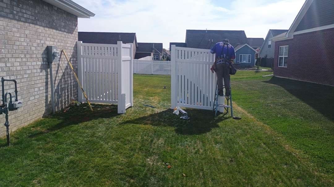An installer works on a white vinyl gate with spaced vertical pickets.