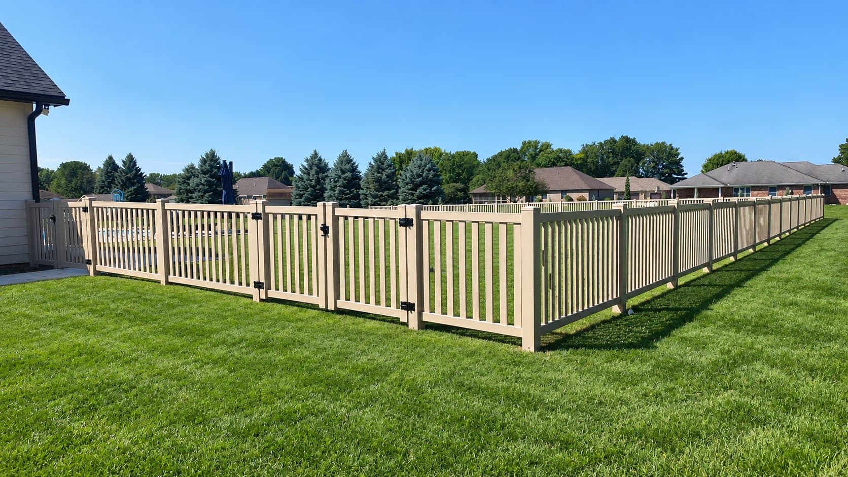 Tan vinyl picket fencing and matching gates border a green lawn.