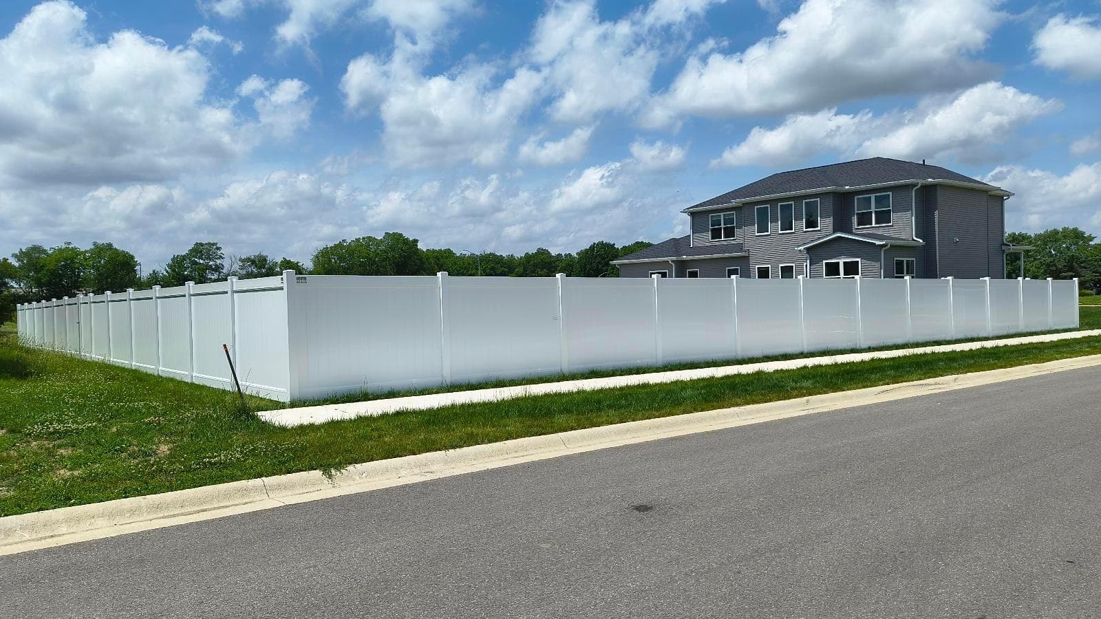 White vinyl privacy fencing traces the lawn beside the street.