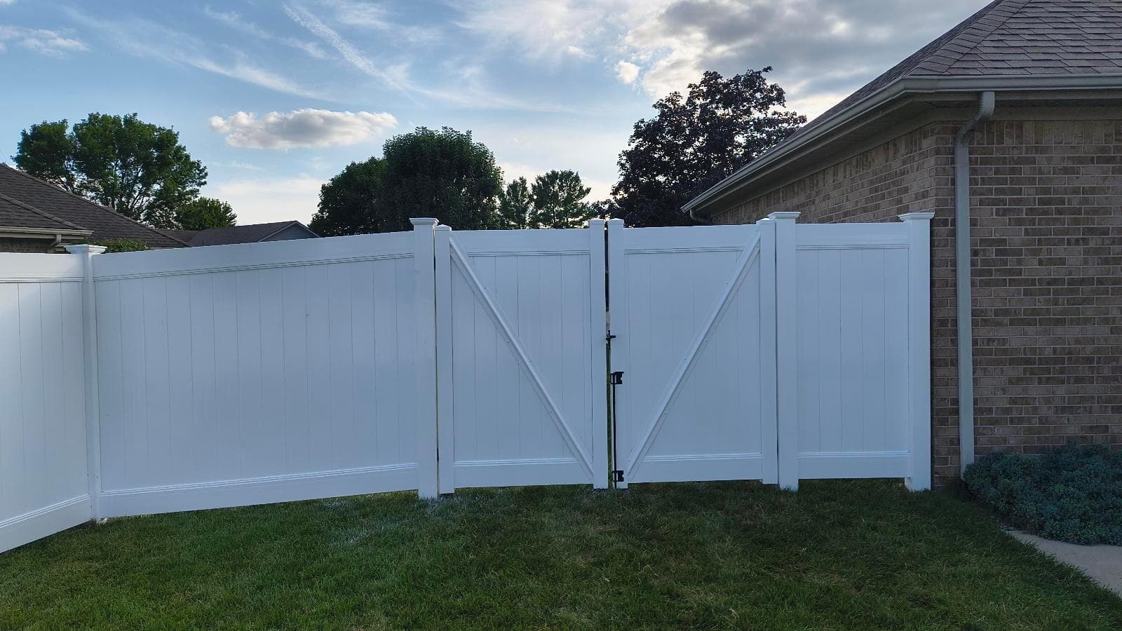 A white vinyl gate with a diagonal brace connects solid panels.