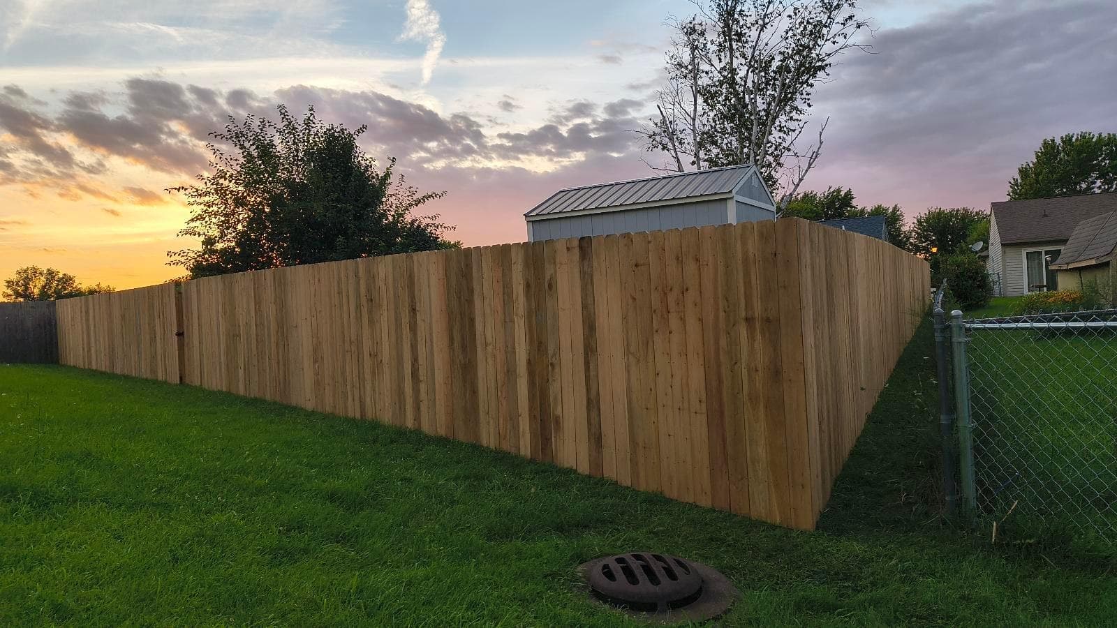 A tall wood fence runs beside the house beneath a sunset sky.