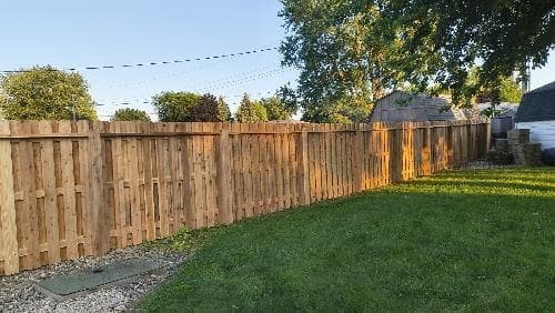 Upright wood boards run between the house and surrounding trees.