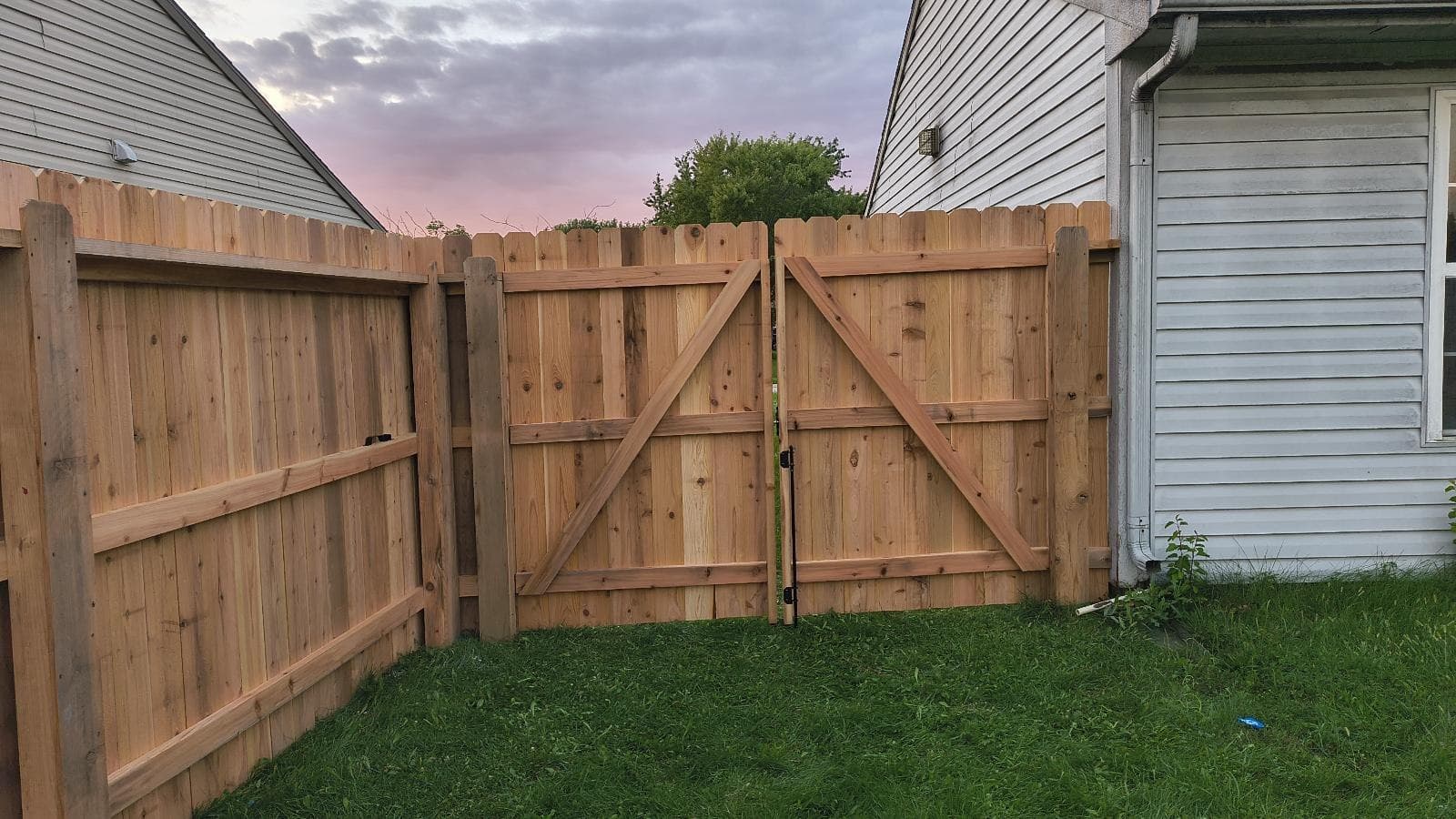 A wood gate with diagonal bracing sits between matching fence sections.