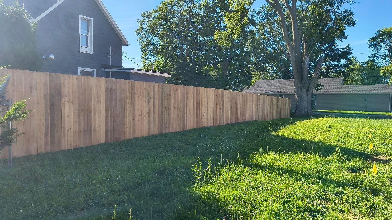 Sunlight falls across a wood fence beside the grass and house.