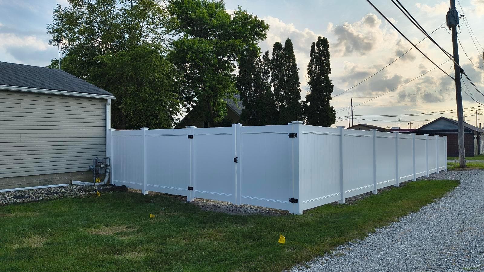 Completed white vinyl privacy fence and matching double gates beside a garage at the Kokomo installation.