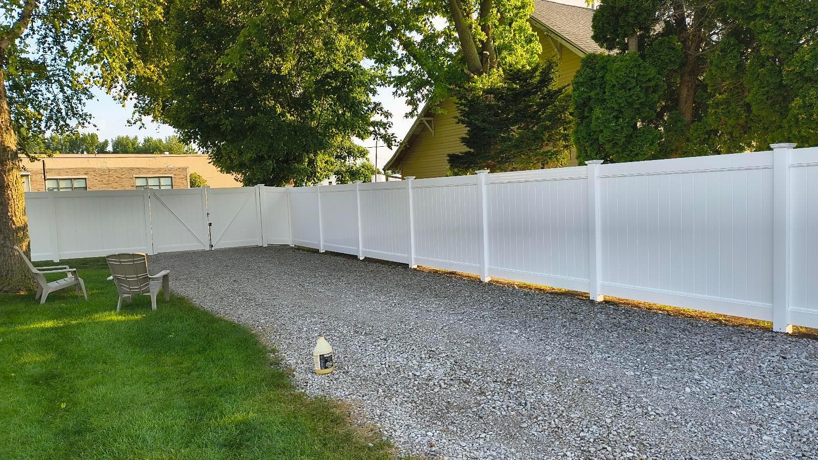 Completed white vinyl privacy fencing enclosing a gravel area beside the house at the Kokomo installation.