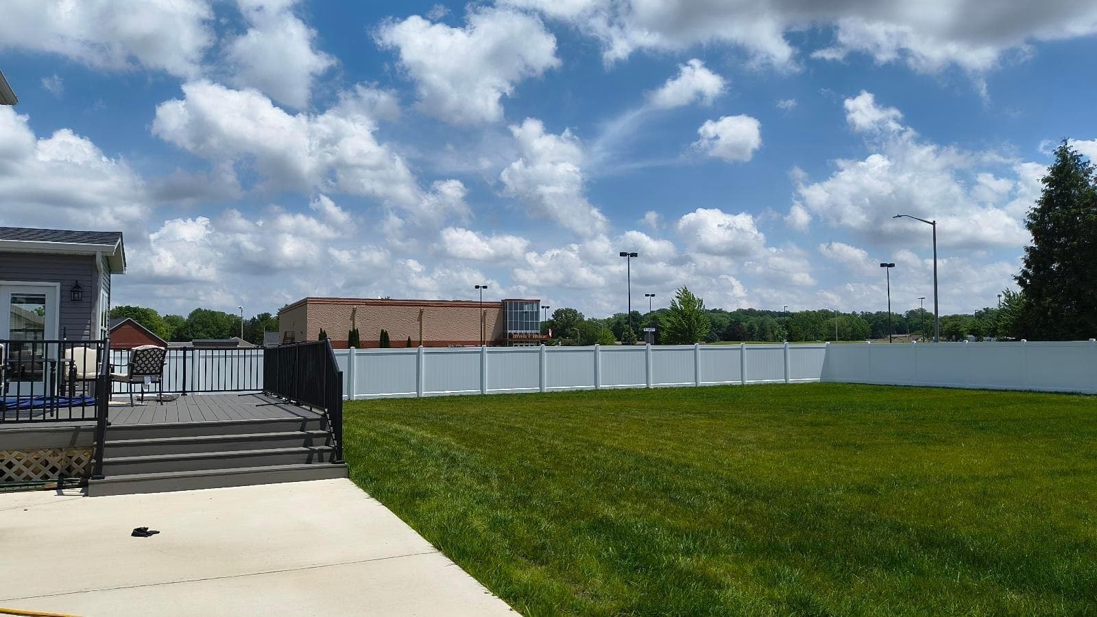 Long white vinyl privacy fence enclosing a broad lawn beyond a patio beneath a blue sky.